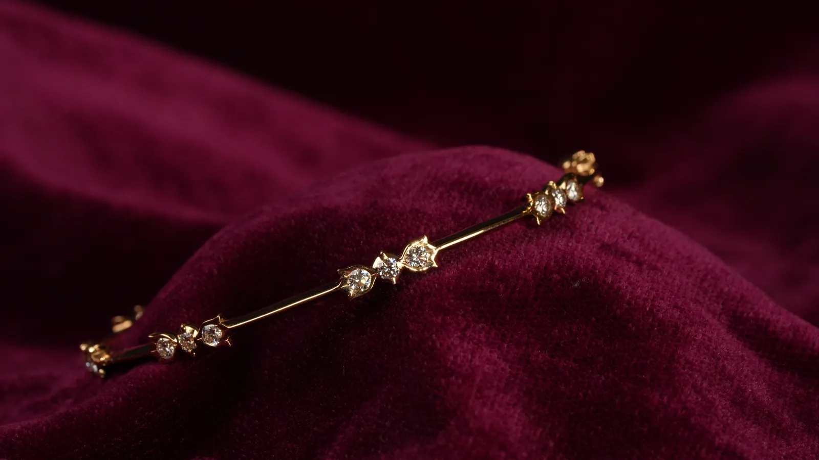 A gold bangle set with diamonds, resting on deep red velvet.
