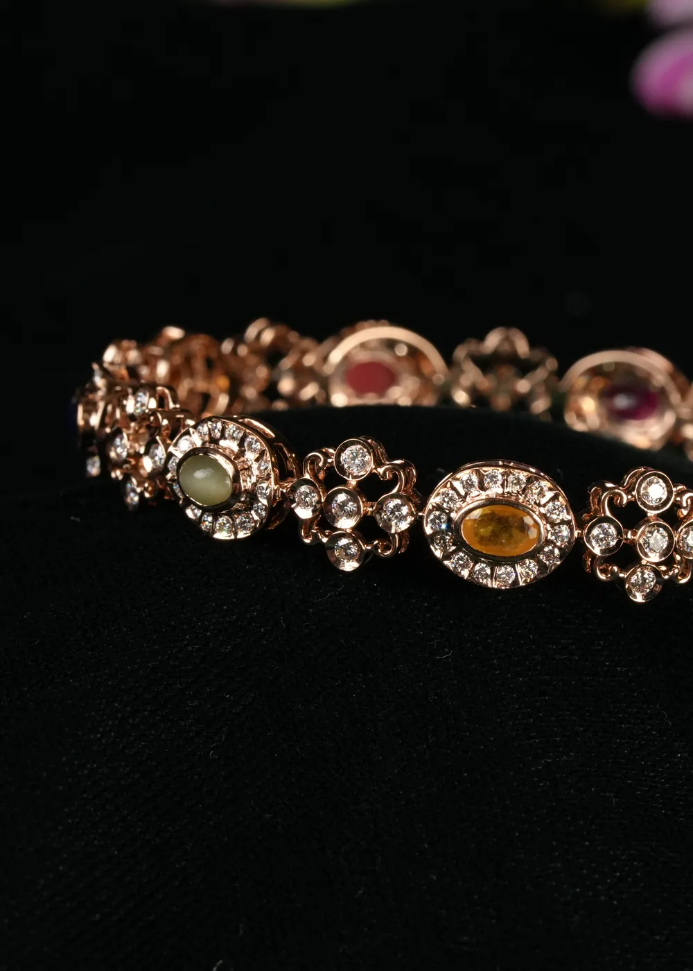 A multi stone bangle on black velvet beneath an orchid.