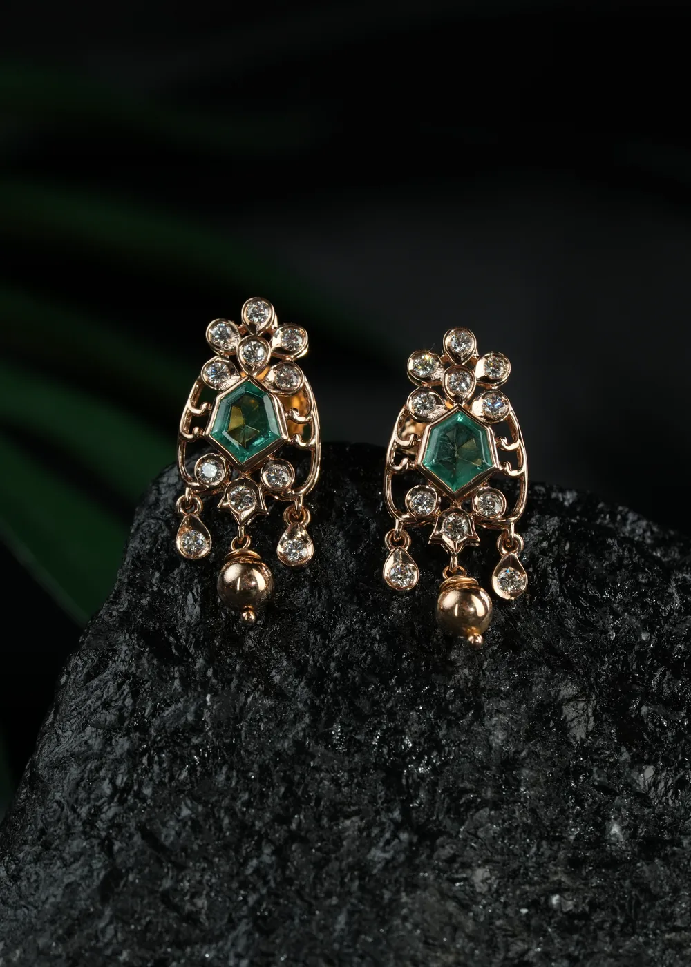 Emerald and diamond drop earrings resting on dark slate.