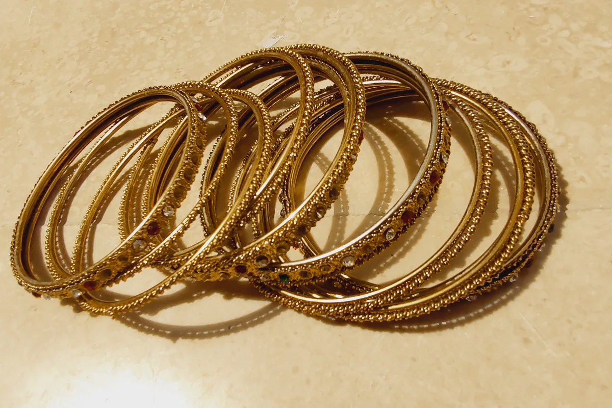 A stack of patterned gold bangles on a cream ground.