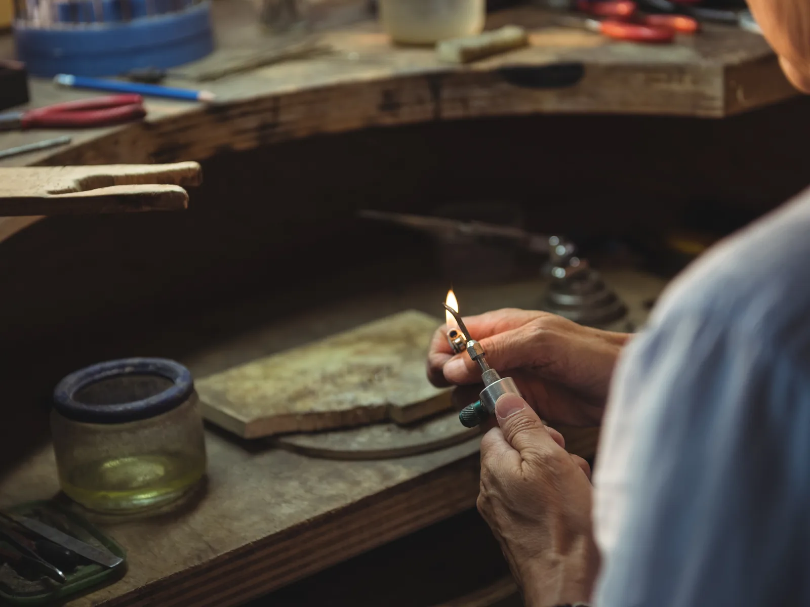 A jeweller at a workbench, holding a small torch to a piece.